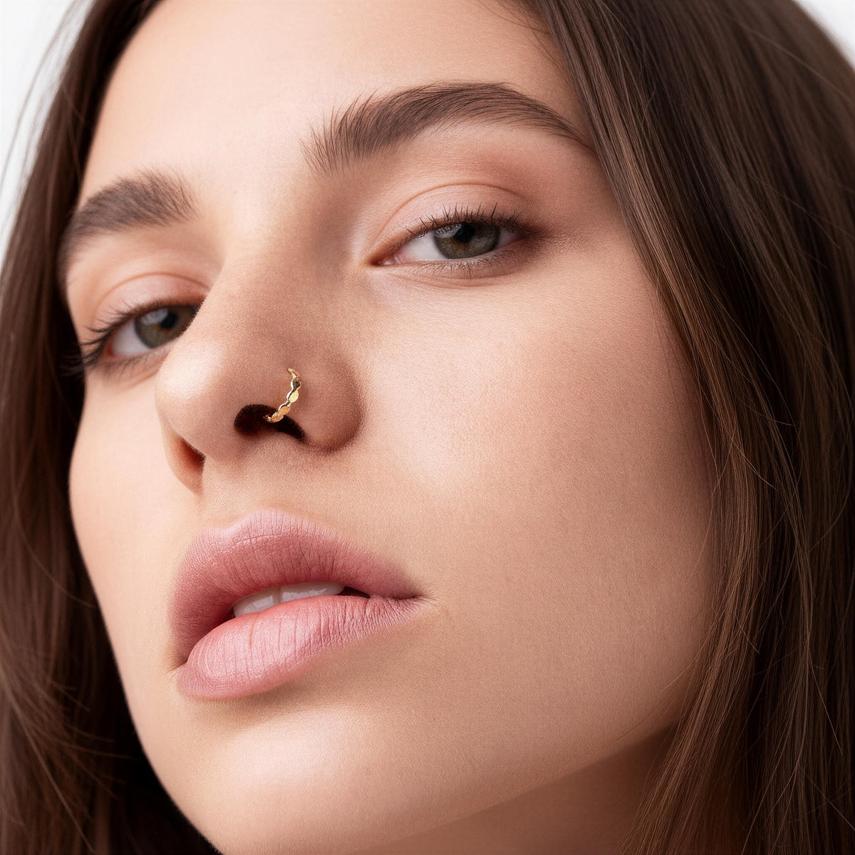 A close-up portrait of a woman with brown hair and a nose ring, looking directly at the camera with a neutral expression.