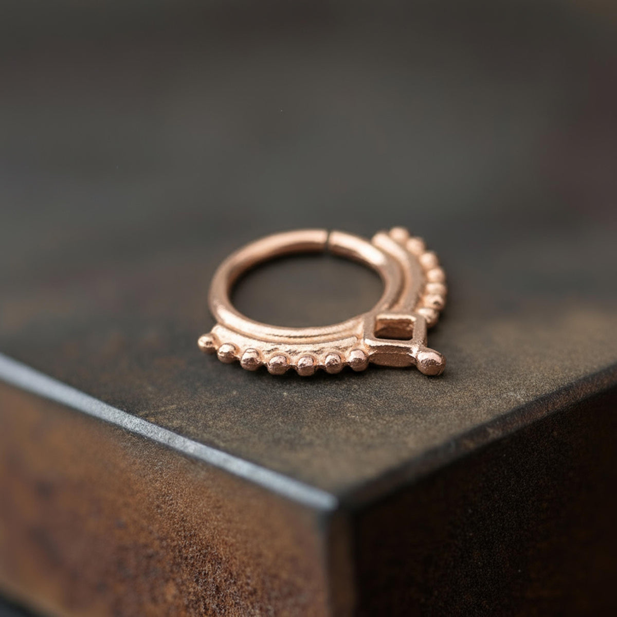 Rose Gold Septum Ring: A close-up image of a copper-colored metal ring or earring resting on a dark surface.