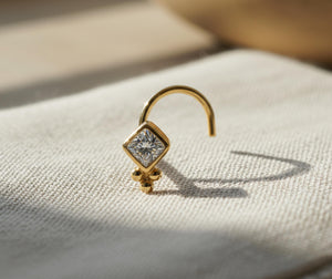 Diamond Nose Stud: A gold nose stud with a diamond-like center stone is displayed on a white fabric surface.
