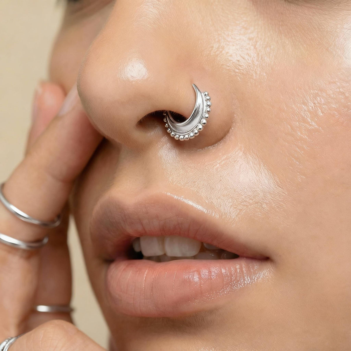 A close-up of a person's face, focusing on their nose and lips, with a nose ring and rings visible.