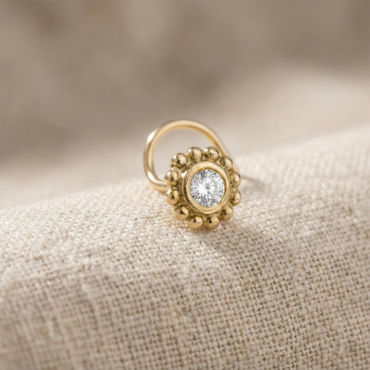 A gold nose ring with a diamond, clear gemstone set in the center