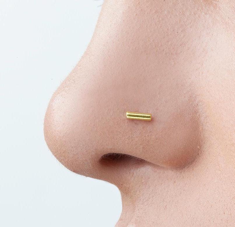 A close-up of a person's nose with a small gold-colored metal piece inserted into it.