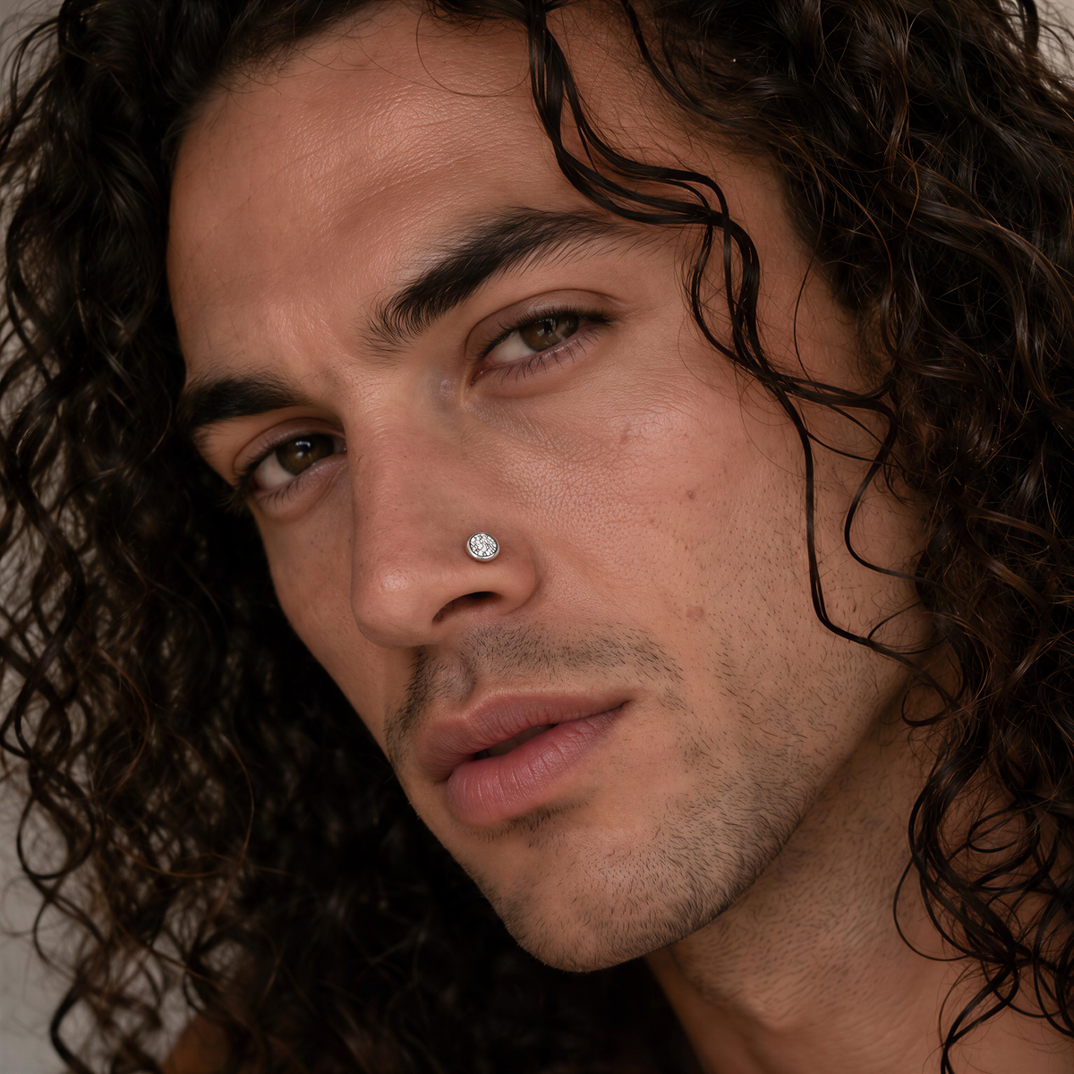 A close-up portrait of a man with long, curly hair and a serious expression.