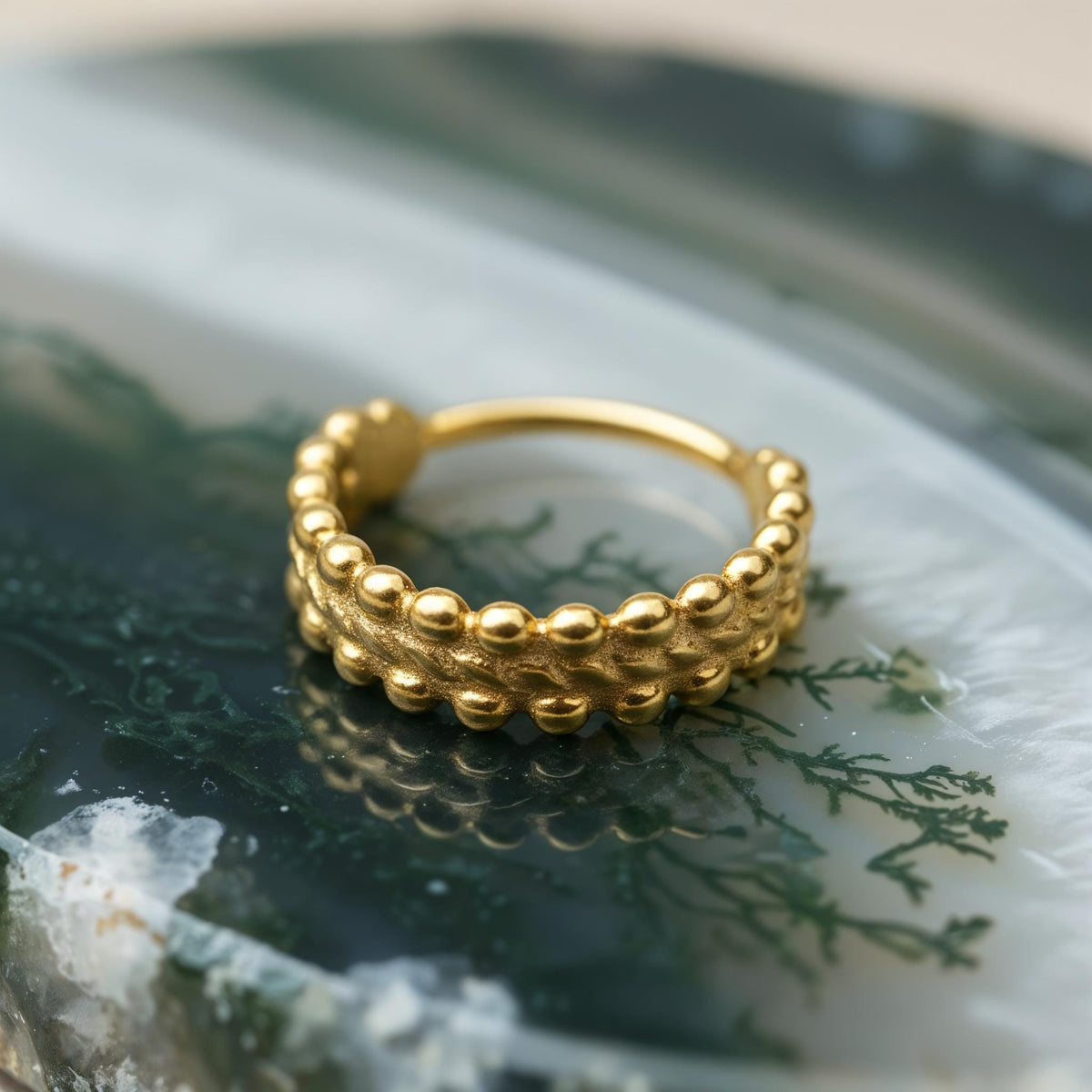 A gold-colored ring with a textured band is displayed on a green and white surface.