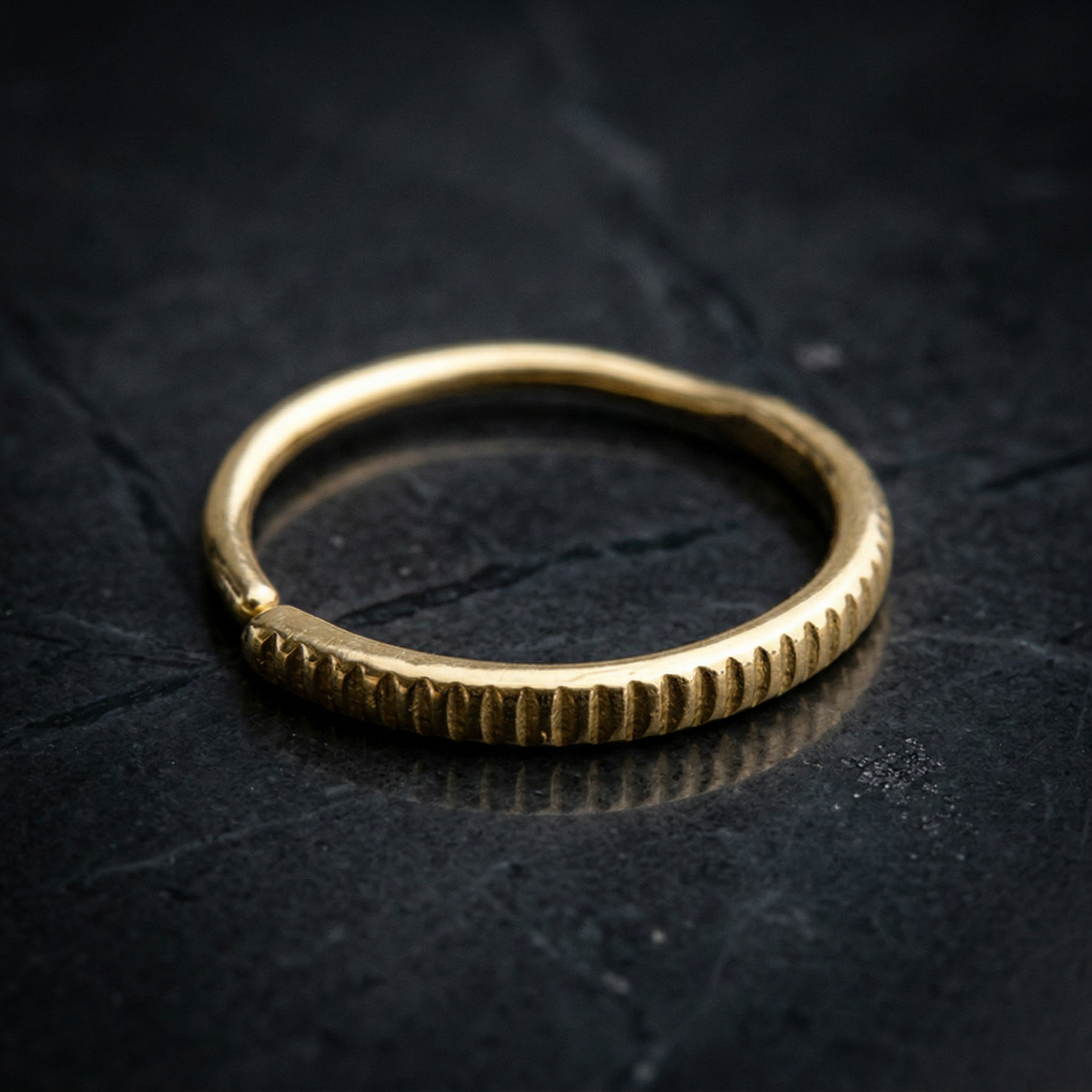 A gold ring with a curved band is resting on a dark surface.
