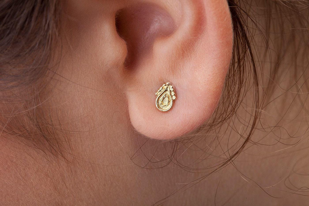 A gold earring with a small, intricate design is visible in the person's ear.