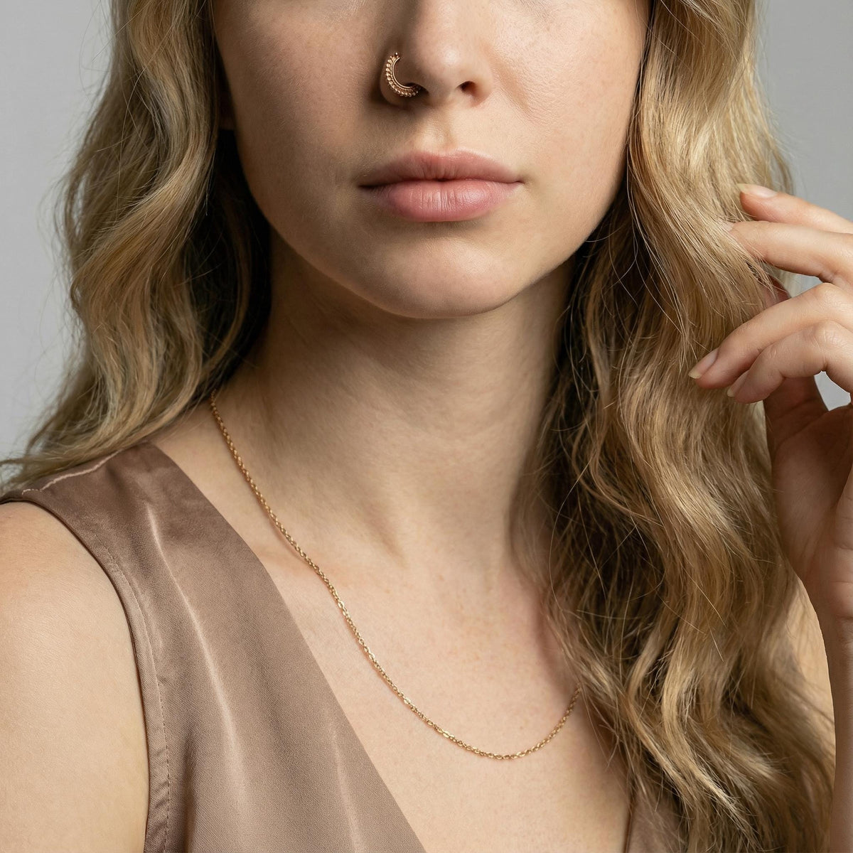 A close-up of a woman's face, focusing on her nose and chin, with her hand resting on her chin. She is wearing a gold necklace and has long, wavy blonde hair.