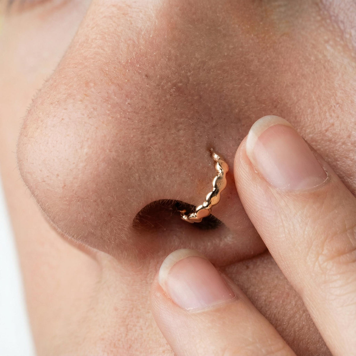 A close-up of a person's nose with a gold hoop earring in it.