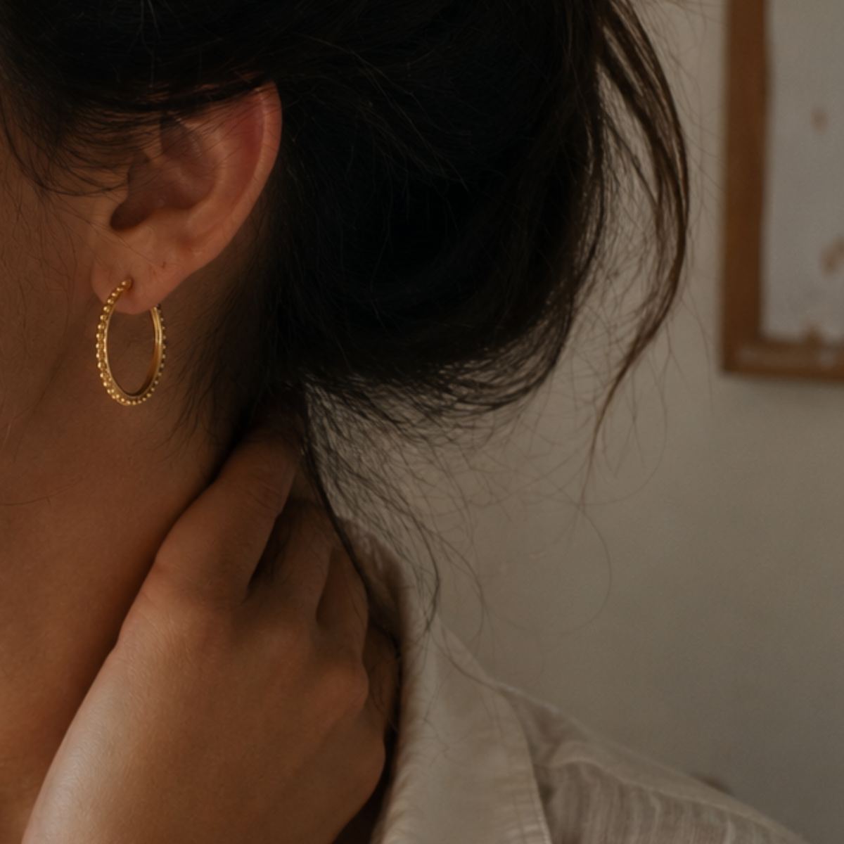 A close-up view of a person's ear and neck, with a gold hoop earring visible.