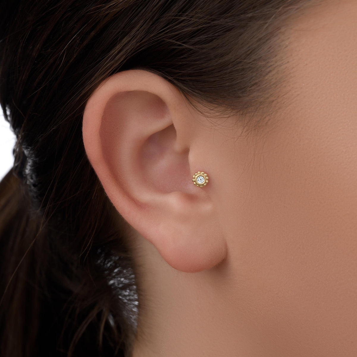 A close-up view of a person's ear with a small gold earring in the earlobe.