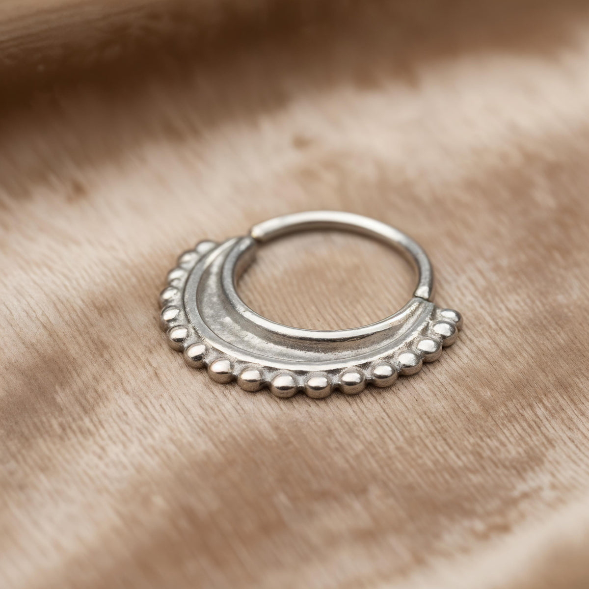 A silver-colored metal ring with a decorative design sits on a textured fabric surface.
