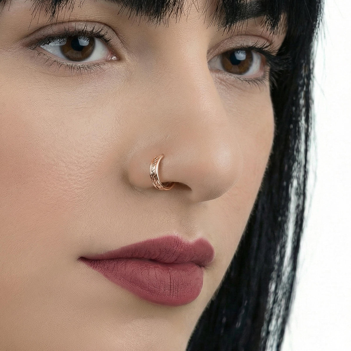 A close-up of a woman's face, focusing on her nose and lips. She has dark hair and is wearing a gold nose ring.