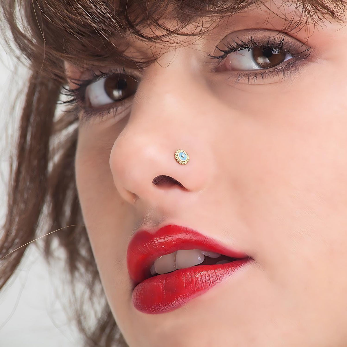A close-up of a woman's face, focusing on her red lips and nose with a gold nose stud.