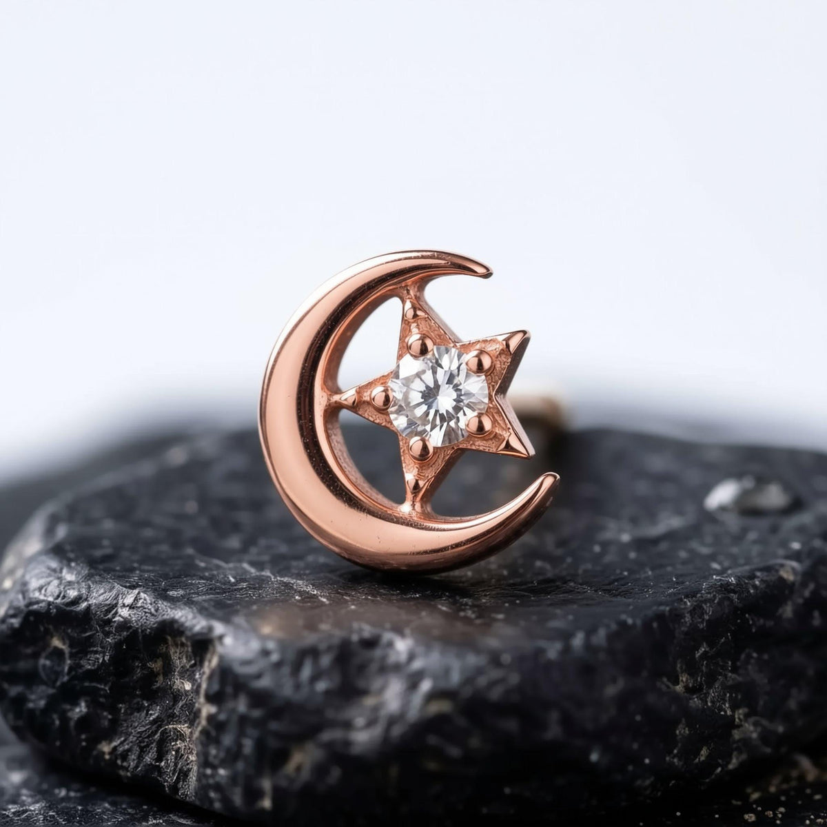 A gold-colored earring with a star-shaped gemstone, resembling a crescent moon, is displayed on a black surface.