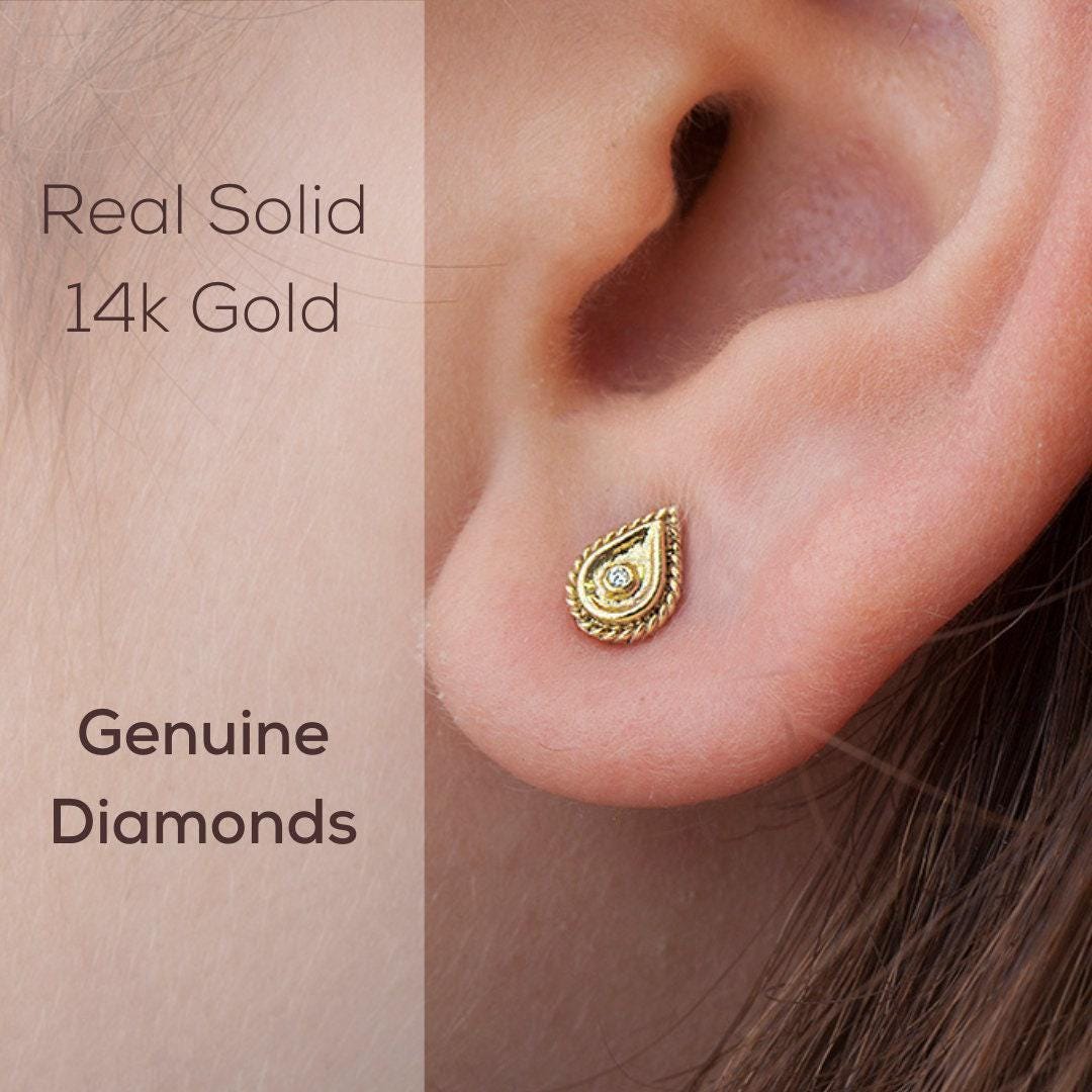 a close-up of a person's ear with a 14k gold earring featuring a small diamond in the center.