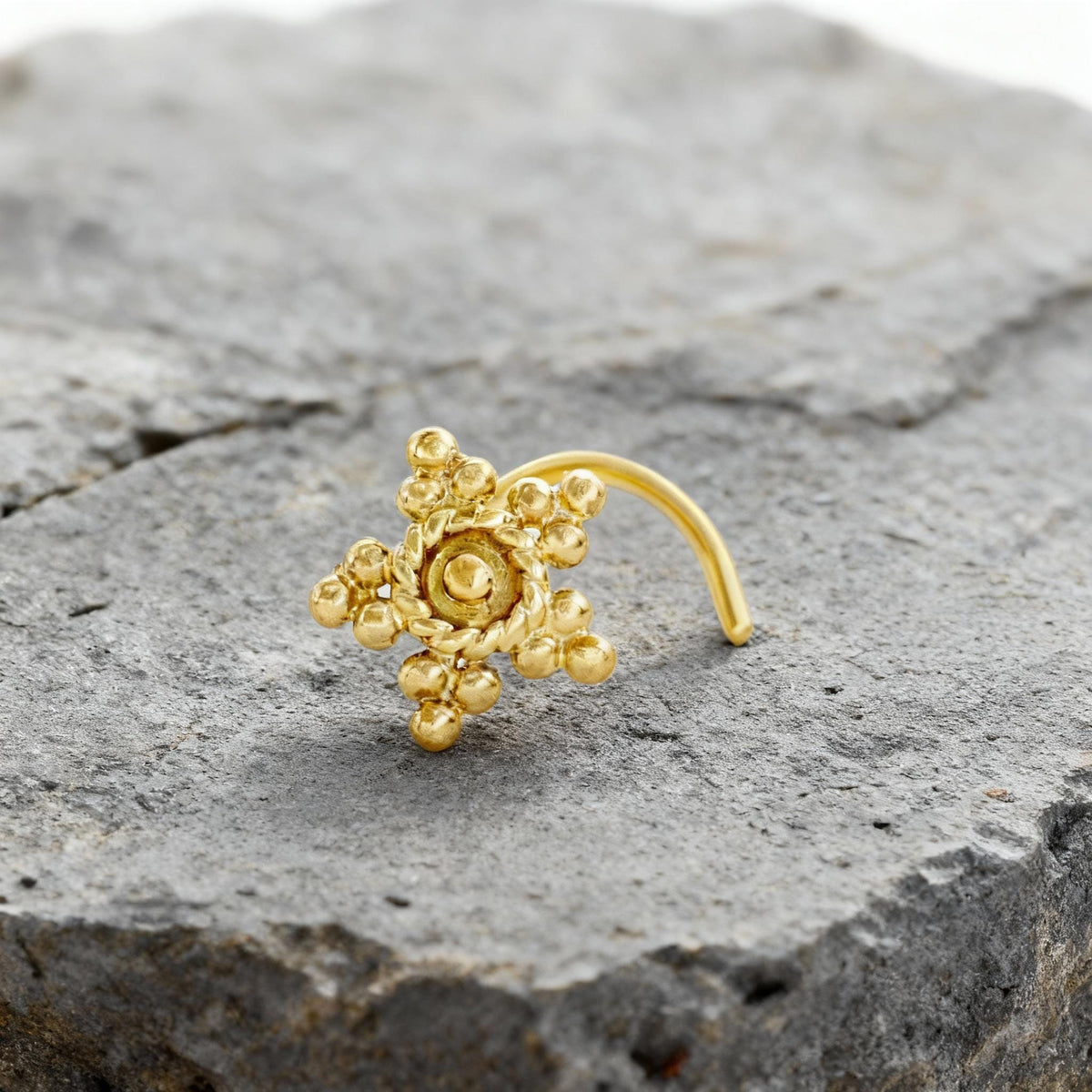 A gold-colored nose ring with a star-shaped design is resting on a gray rock.