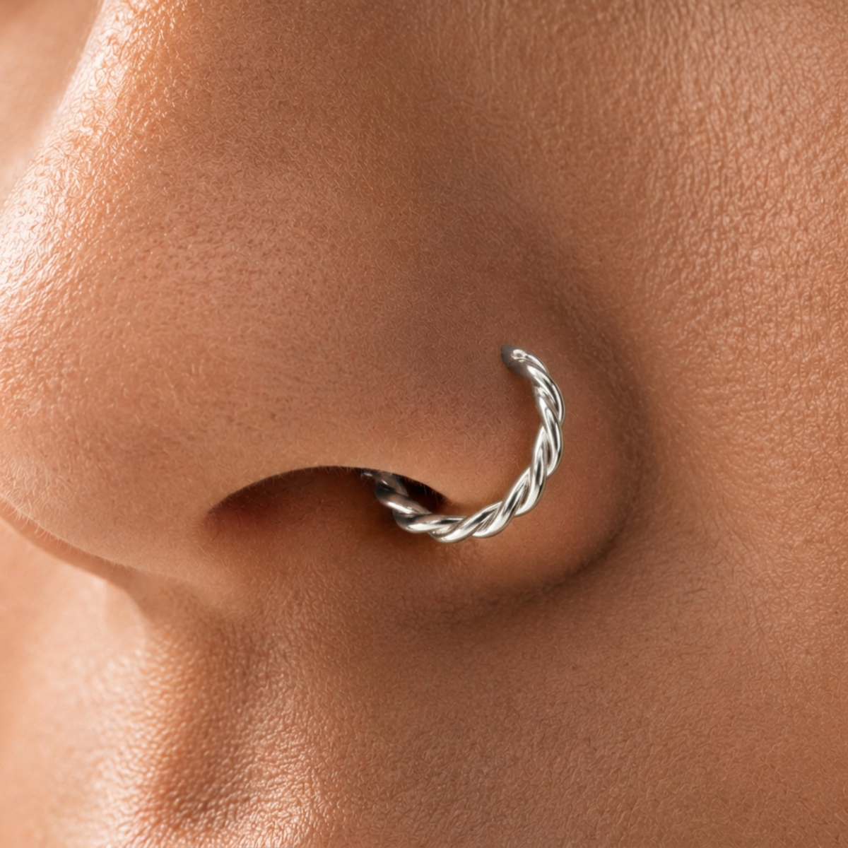 A close-up of a person's nose with a silver twisted nose ring.