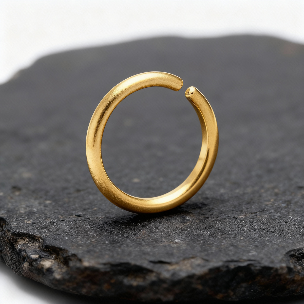 A gold ring with a twisted shape is resting on a dark surface.