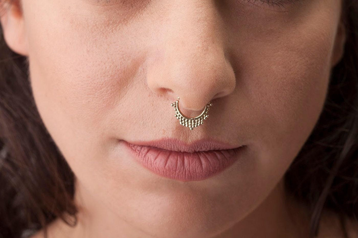 A close-up of a woman's face, focusing on her nose and lips. She is wearing a decorative nose ring.