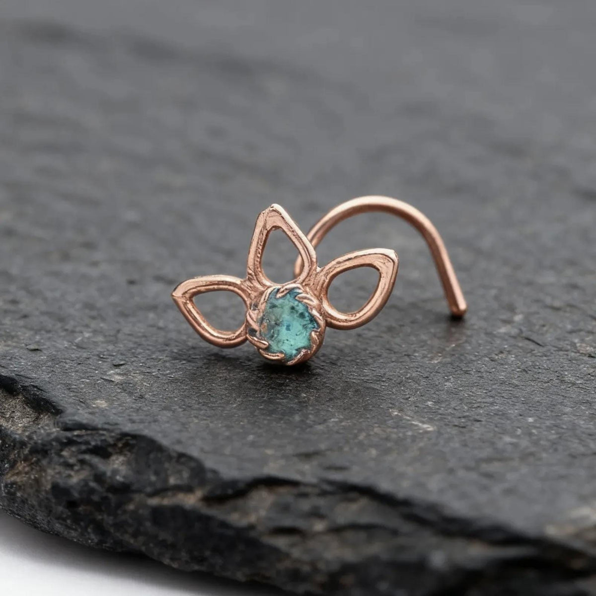 A copper-colored nose ring with a blue gemstone is displayed on a dark gray surface.