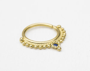 Indian Nose Ring: A gold-colored nose ring with a blue gemstone, possibly a sapphire, is shown against a white background.