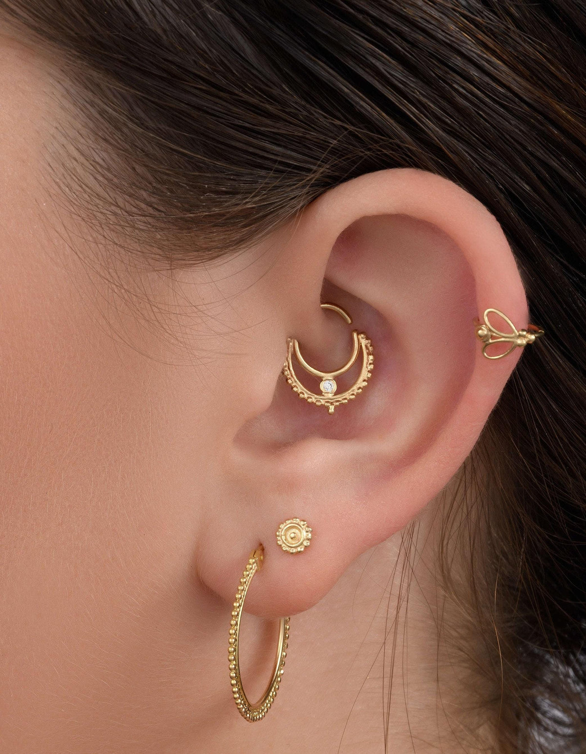 A close-up view of a person's ear adorned with multiple gold earrings, including hoop earrings and a crescent moon earring.