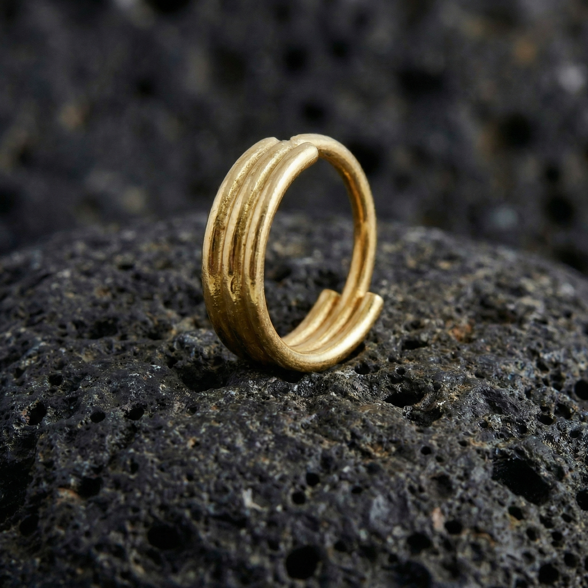 A gold ring with three concentric bands is resting on a dark, rocky surface.
