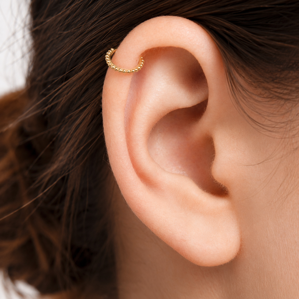 A close-up view of a person's ear with a gold-colored earring in the earlobe.