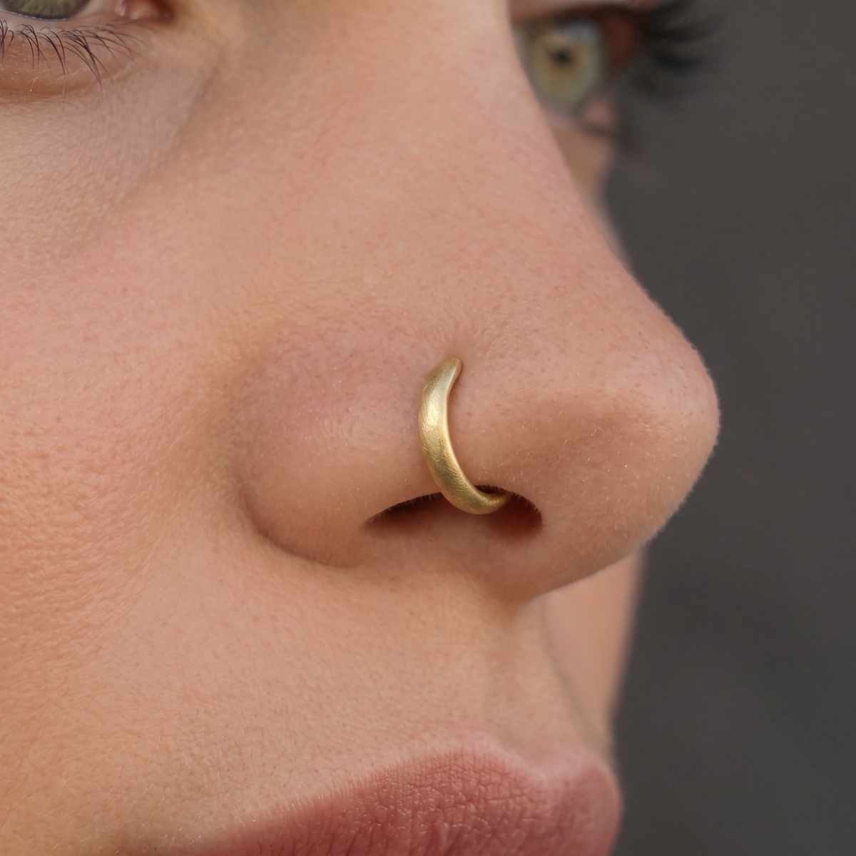 A close-up of a person's nose and mouth, with a gold nose ring visible.