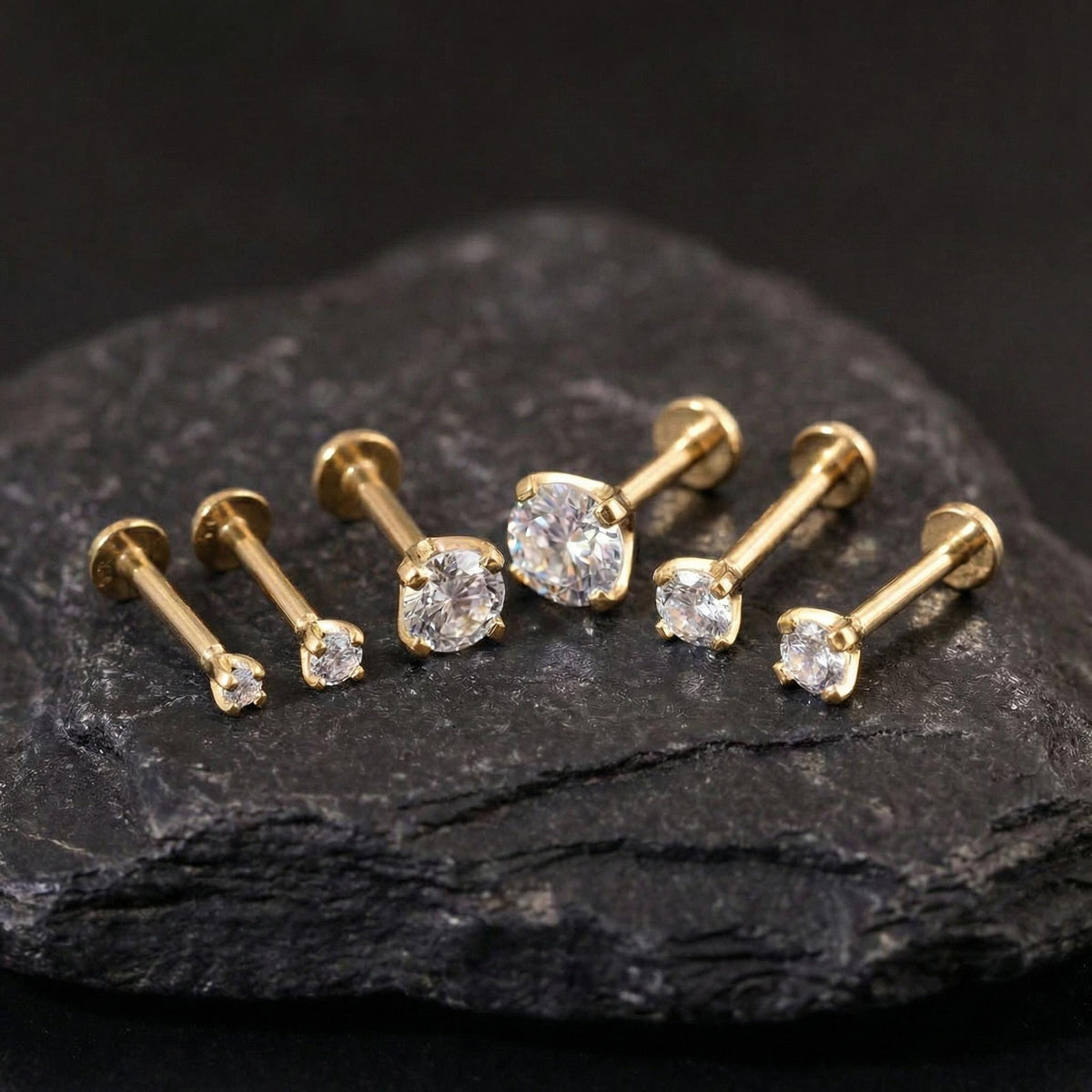 A collection of gold-colored diamond earrings is displayed on a dark surface, with the largest earrings in the center and smaller ones surrounding them.