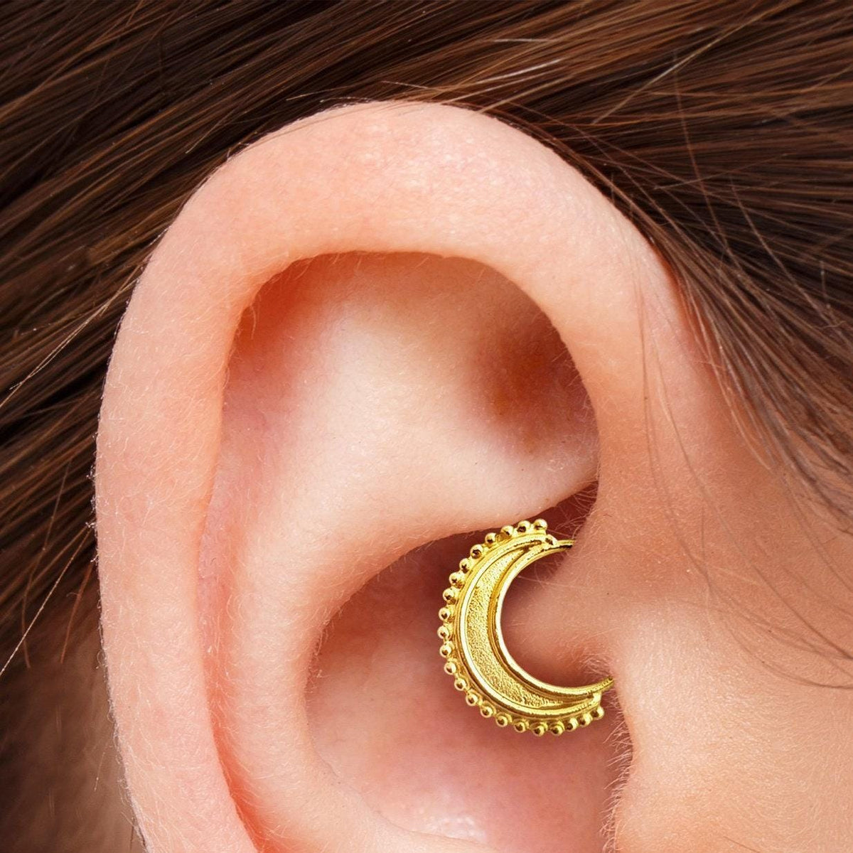 A close-up view of a person's ear with a gold-colored earring in the earlobe.