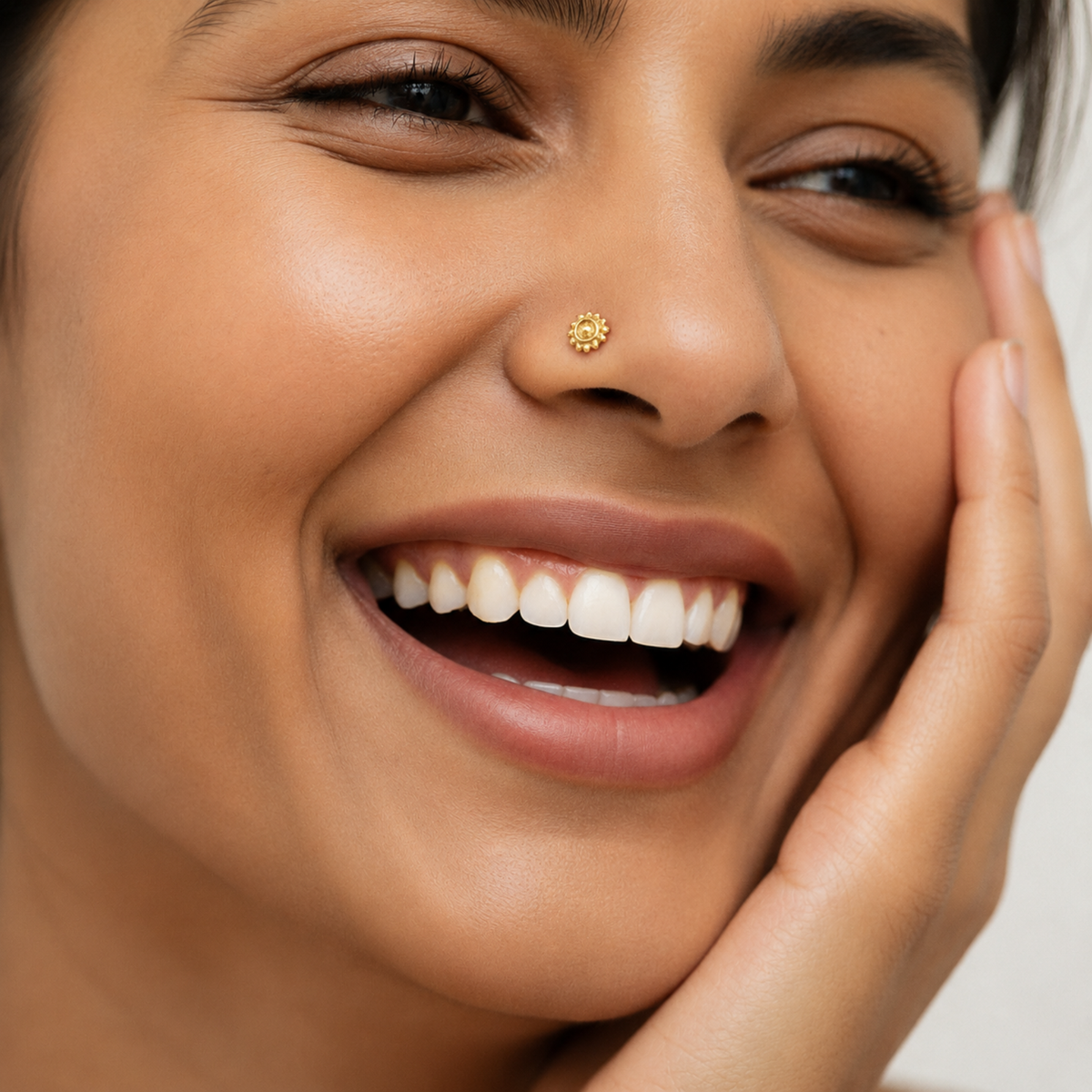 A close-up of a smiling woman's face, with her eyes closed and her hand resting on her cheek.