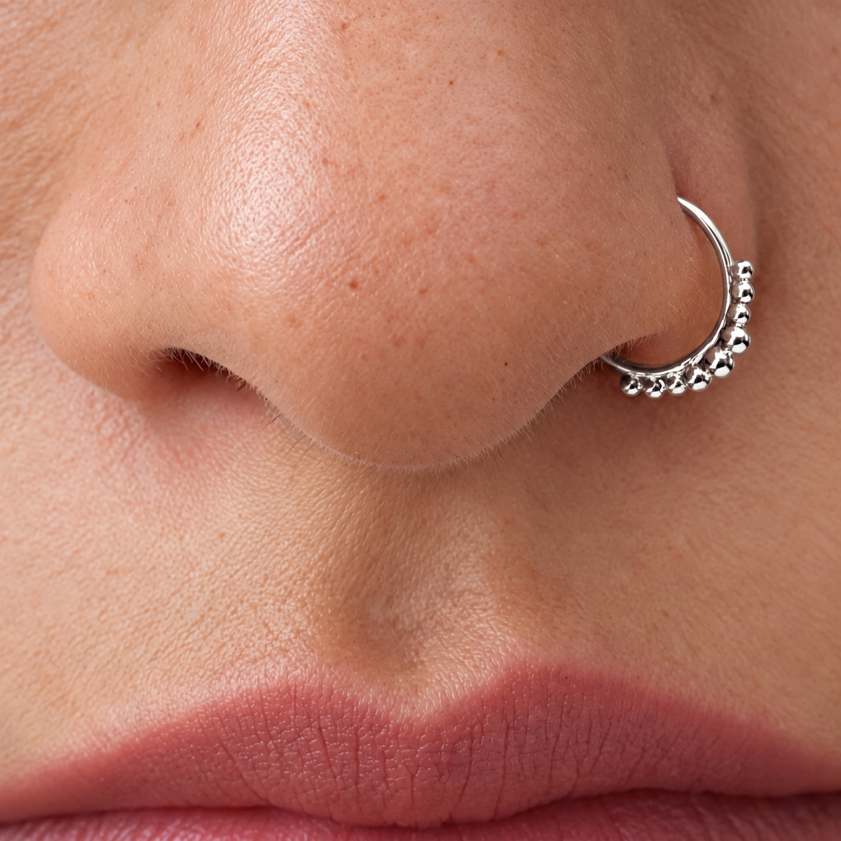 A close-up of a person's nose and lips, with a silver hoop earring visible.