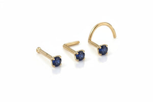 Three gold-colored nose studs with blue gemstones are displayed against a white background.
