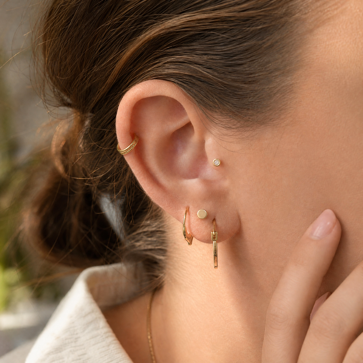 A close-up of a person's ear adorned with multiple gold earrings, including a hoop earring and a stud earring.