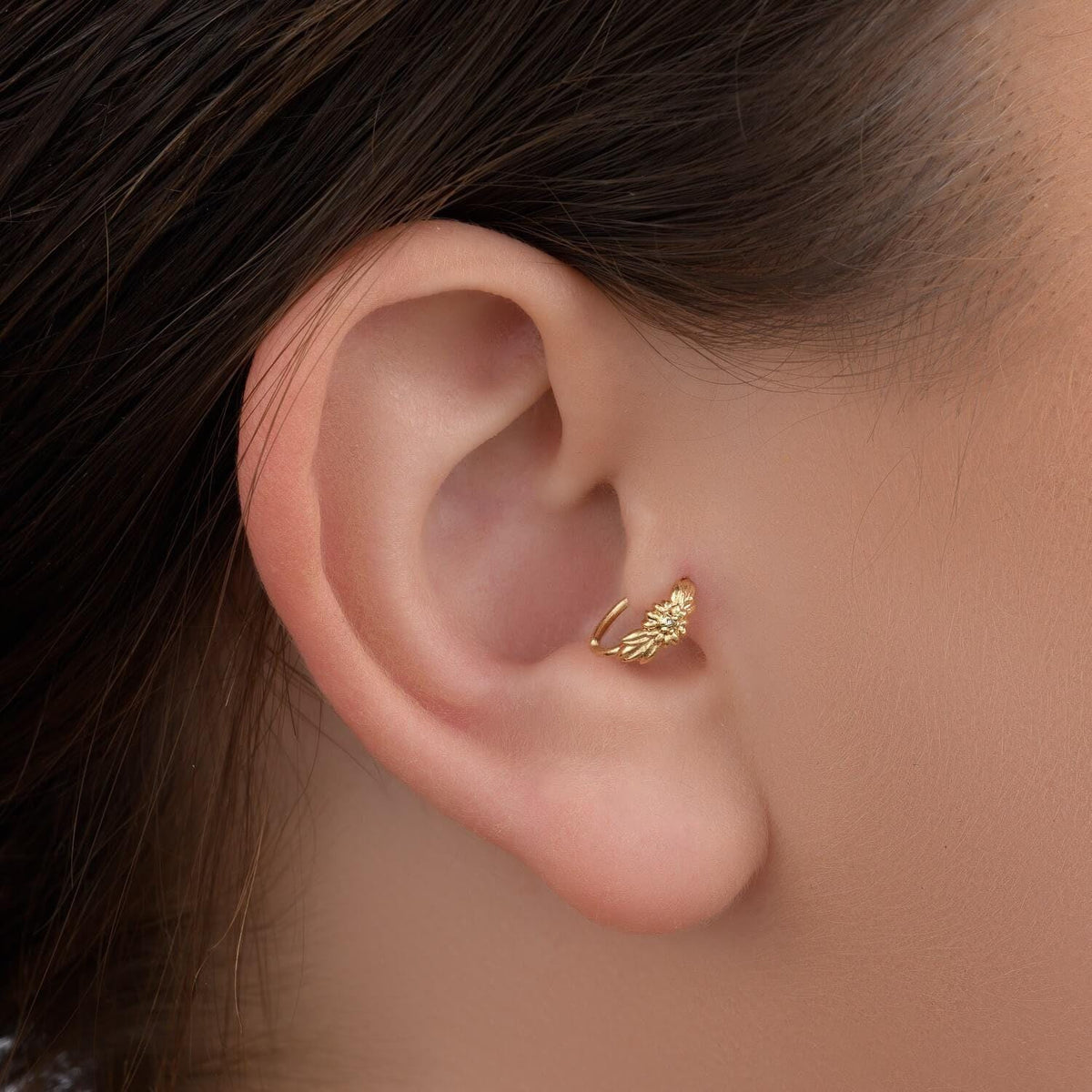 A close-up view of a person's ear with a gold-colored earring or ear cuff.