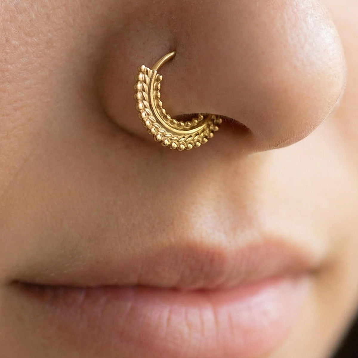 A close-up of a person's nose and mouth, with a gold-colored ornate nose ring prominently displayed.