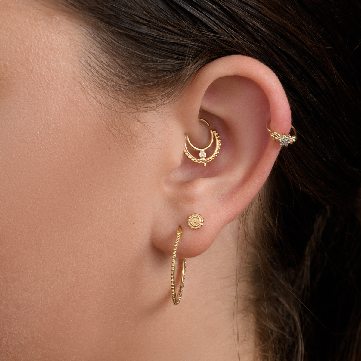 A close-up of a person's ear adorned with multiple gold earrings, including a hoop earring, a stud earring, and a ring.