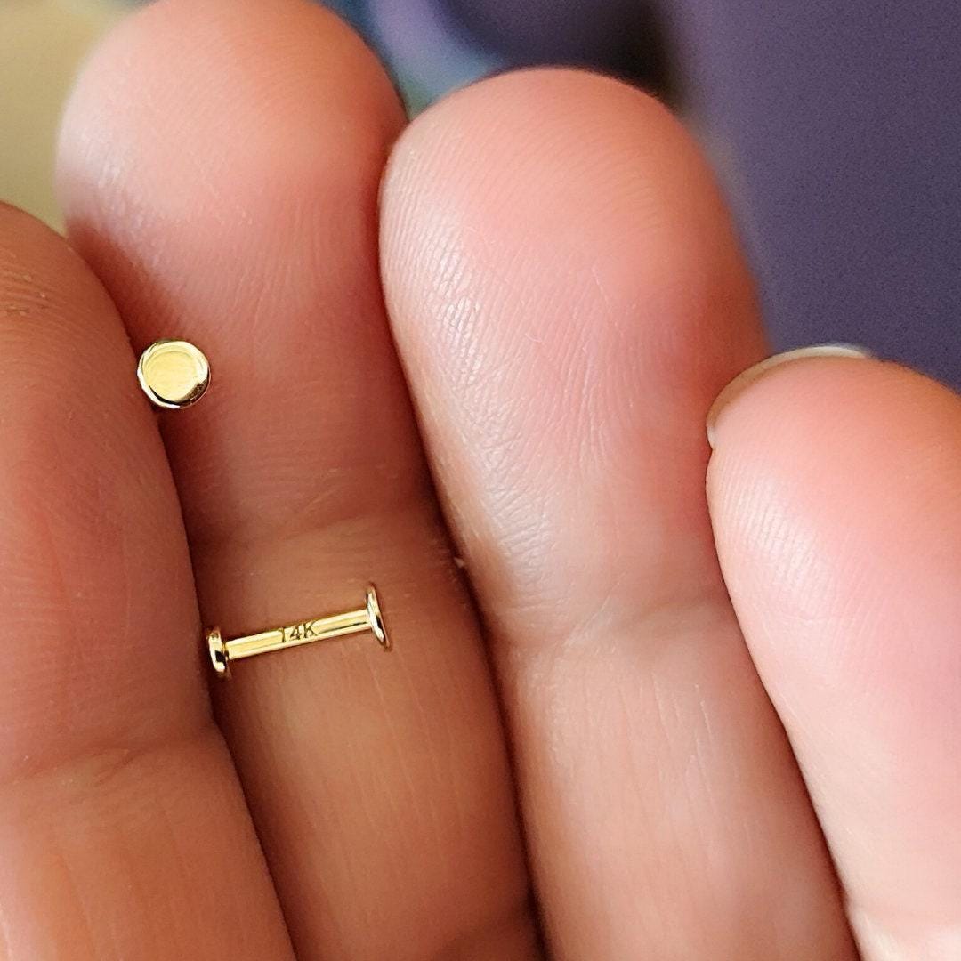 A close-up image of a person's fingers holding a small gold-colored earring and a small gold-colored pin.
