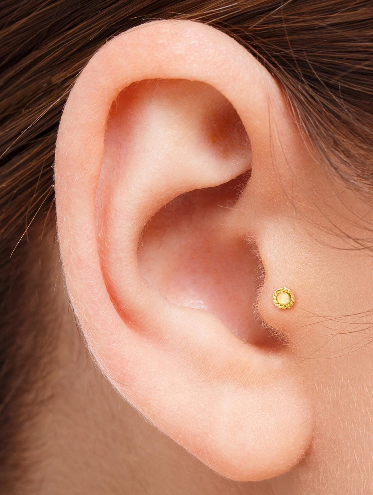 A close-up view of an ear with a gold earring in the earlobe.