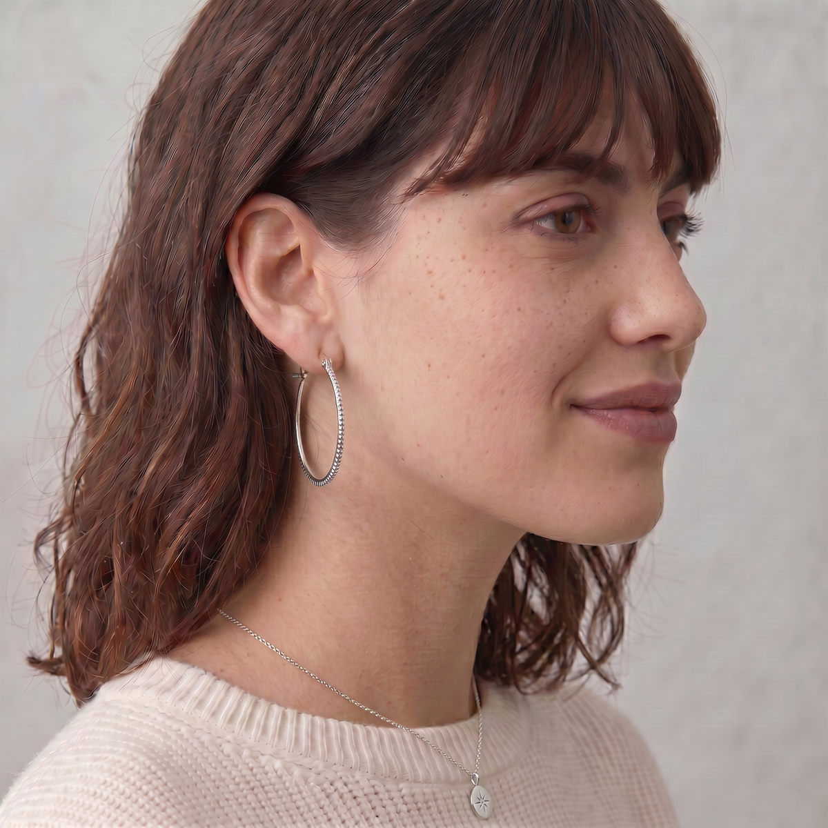 A woman with long brown hair wearing a white sweater and hoop earrings, smiling at the camera.