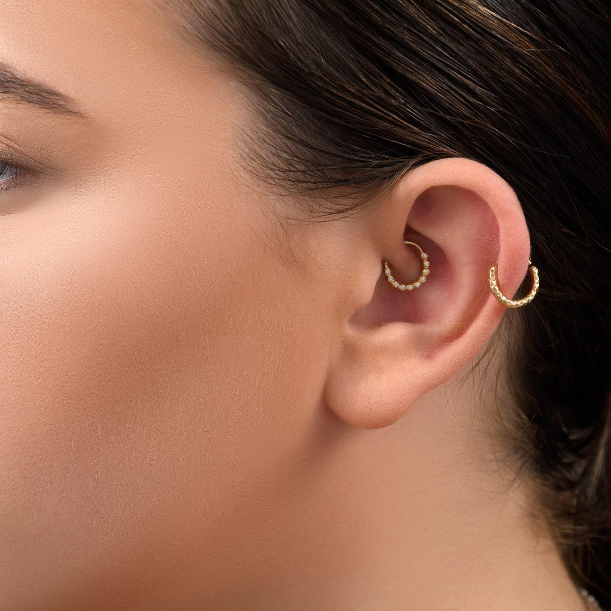 A close-up of a person's ear with a gold hoop earring in their ear.