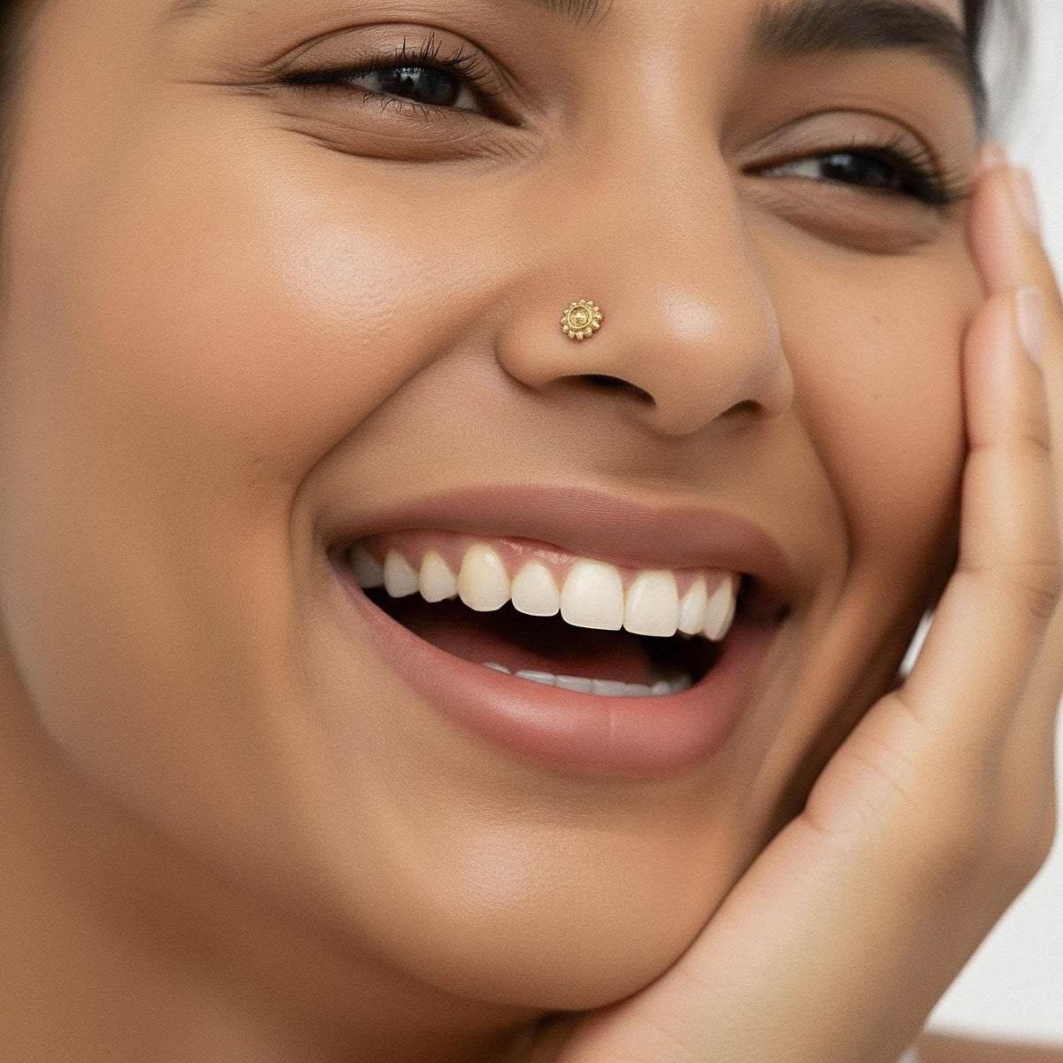 A close-up of a smiling woman's face, with her eyes closed and her hand resting on her cheek.