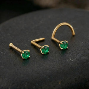 three gold-colored earrings with green gemstones, placed on a dark surface.