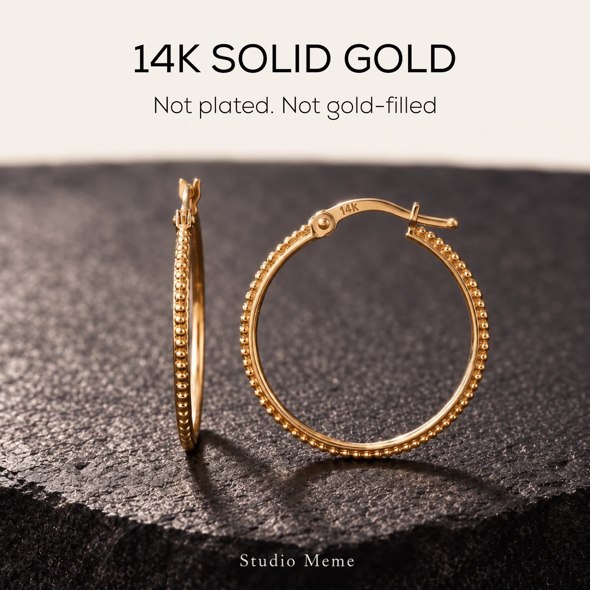 A pair of 14K solid gold earrings with a textured bezel design, placed on a dark surface.