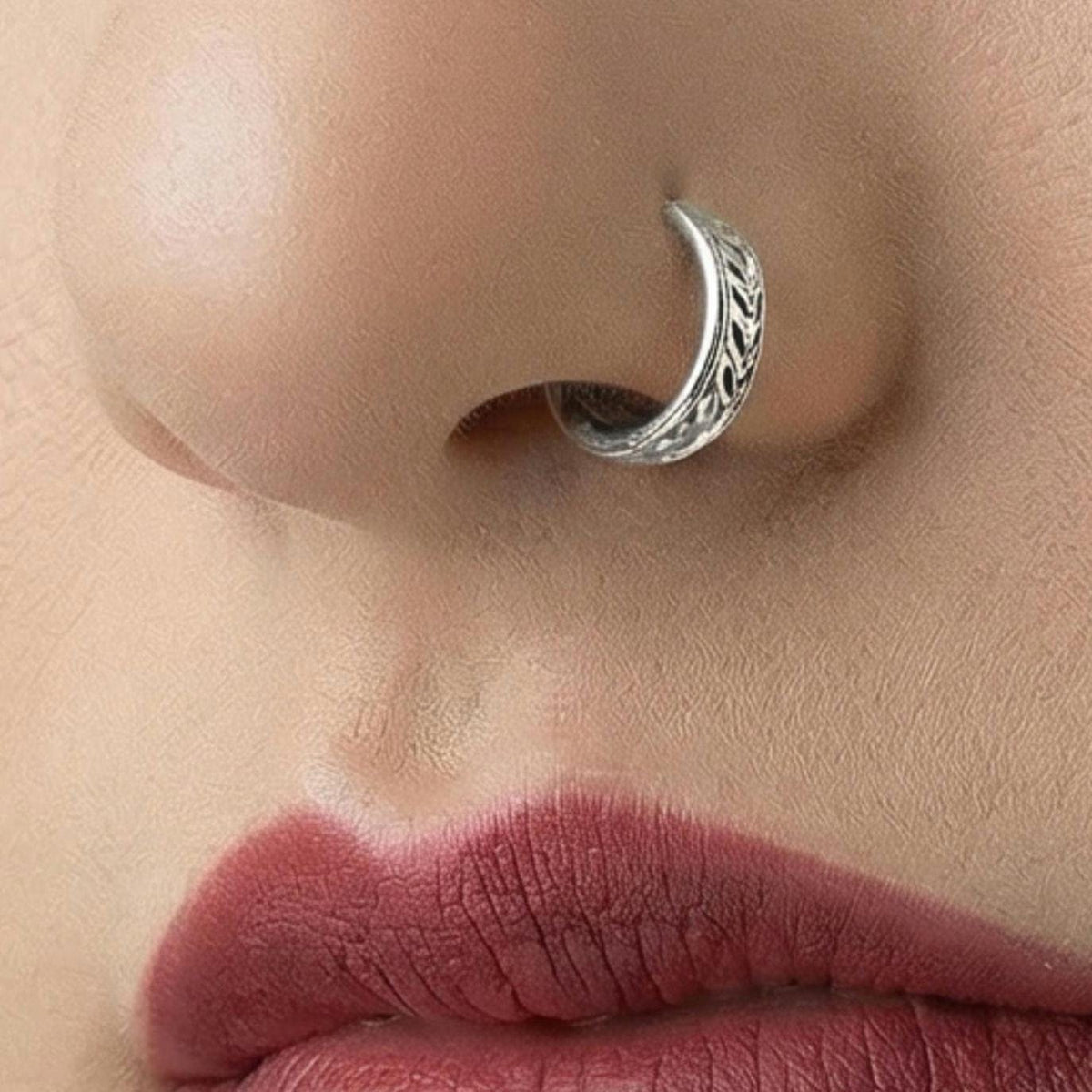 A close-up of a woman's face, focusing on her lips and nose. She has dark hair and is wearing a silver nose ring.