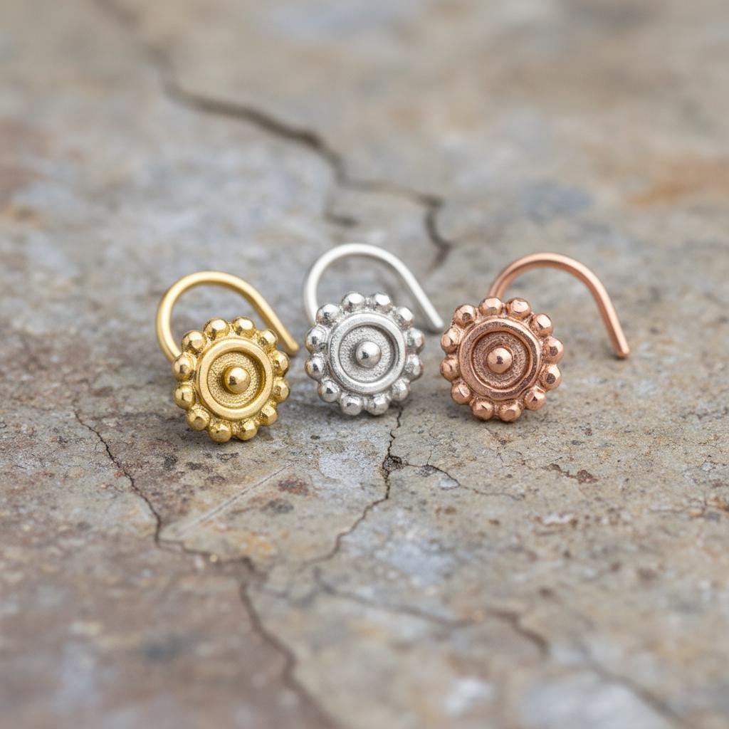 Three colorful nose studs are arranged on a textured surface.
