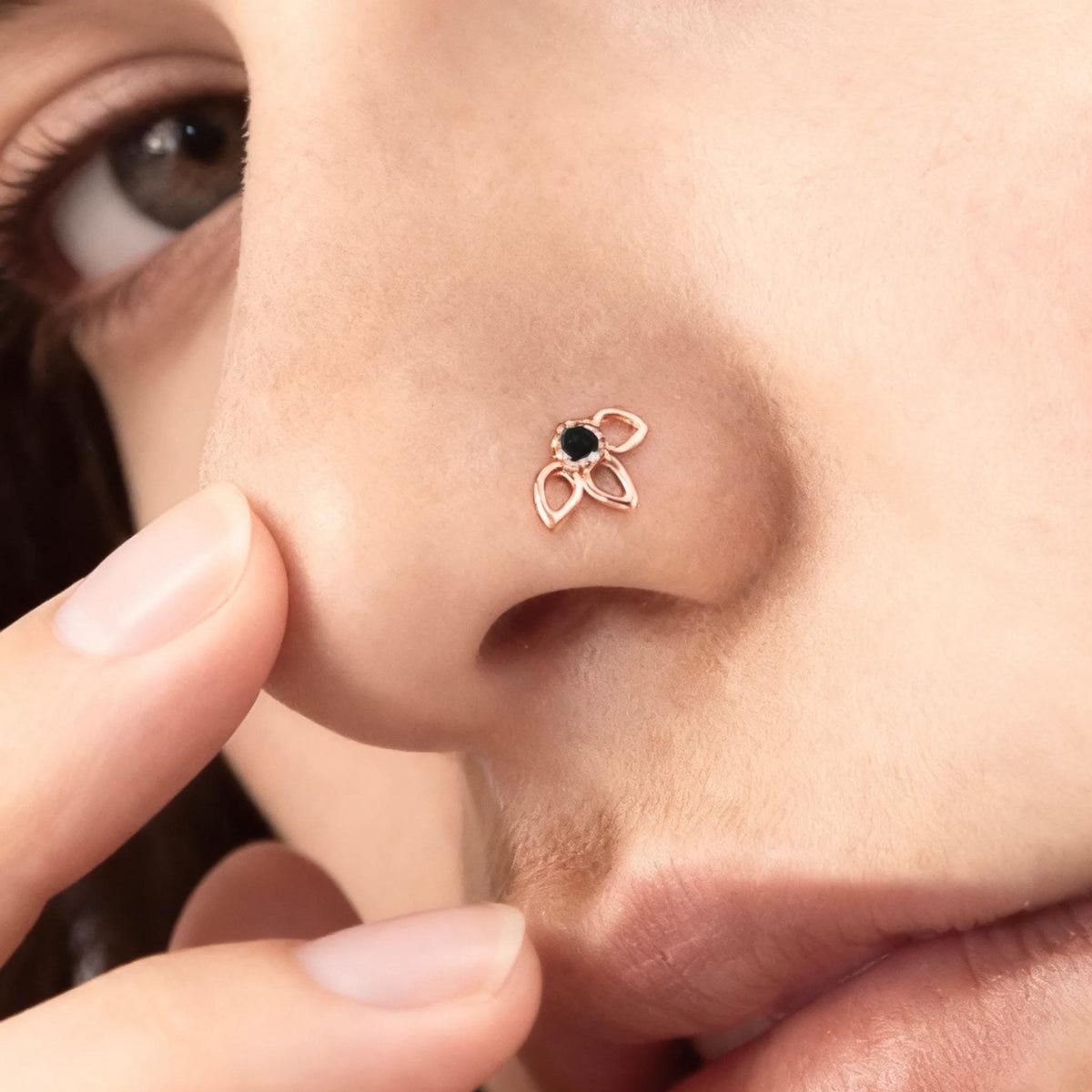 Flower Nose Stud: A close-up of a person's nose with a small, ornate nose ring featuring a black gemstone.