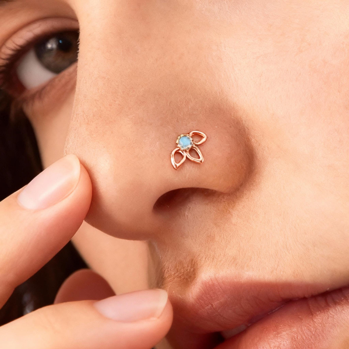 A close-up of a person's nose with a small, delicate nose ring featuring a blue gemstone.