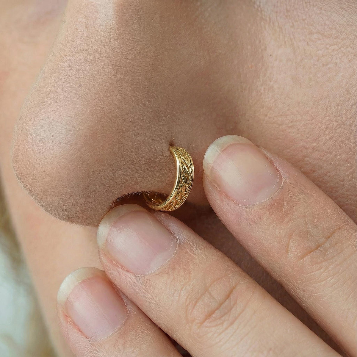 A close-up of a person's nose and fingers, with a gold-colored nose ring visible.